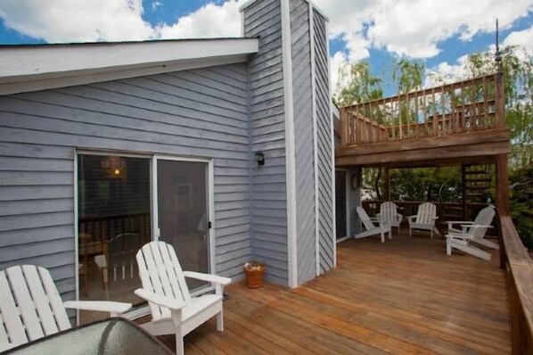 A wooden deck with white chairs and a glass door leading to a covered area. - Pelican Perch (Rear Unit) (Virginia Beach)