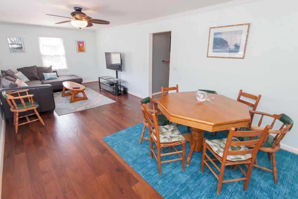 A living room with a wooden dining table, chairs, a sofa, a TV, and a ceiling fan.