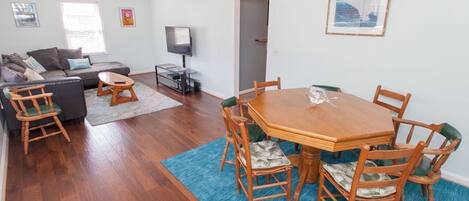 A living room with a wooden dining table, chairs, a sofa, a TV, and a ceiling fan.