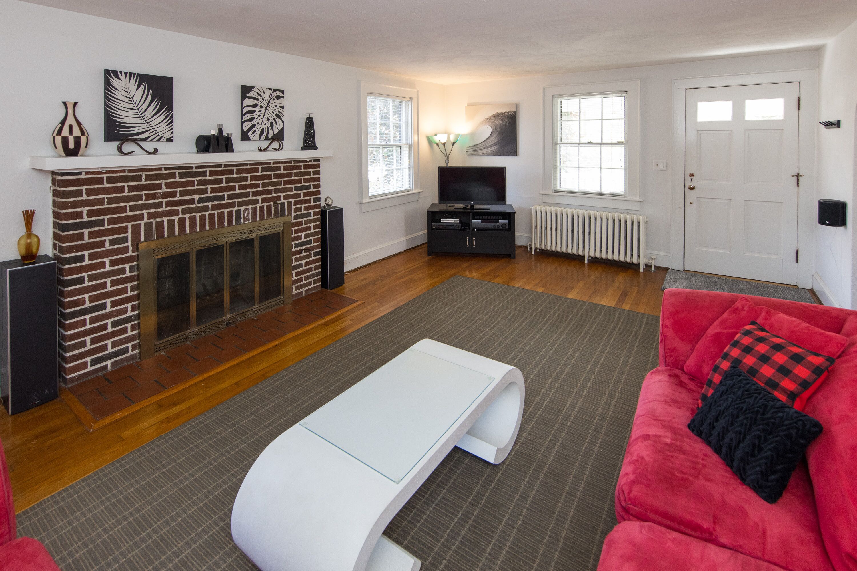 A living room with a brick fireplace, a flat-screen TV, a red sofa, and a white coffee table.