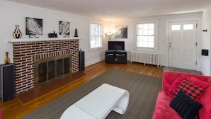 Un salón con chimenea de ladrillo, televisor de pantalla plana, sofá rojo y una mesa de centro blanca.