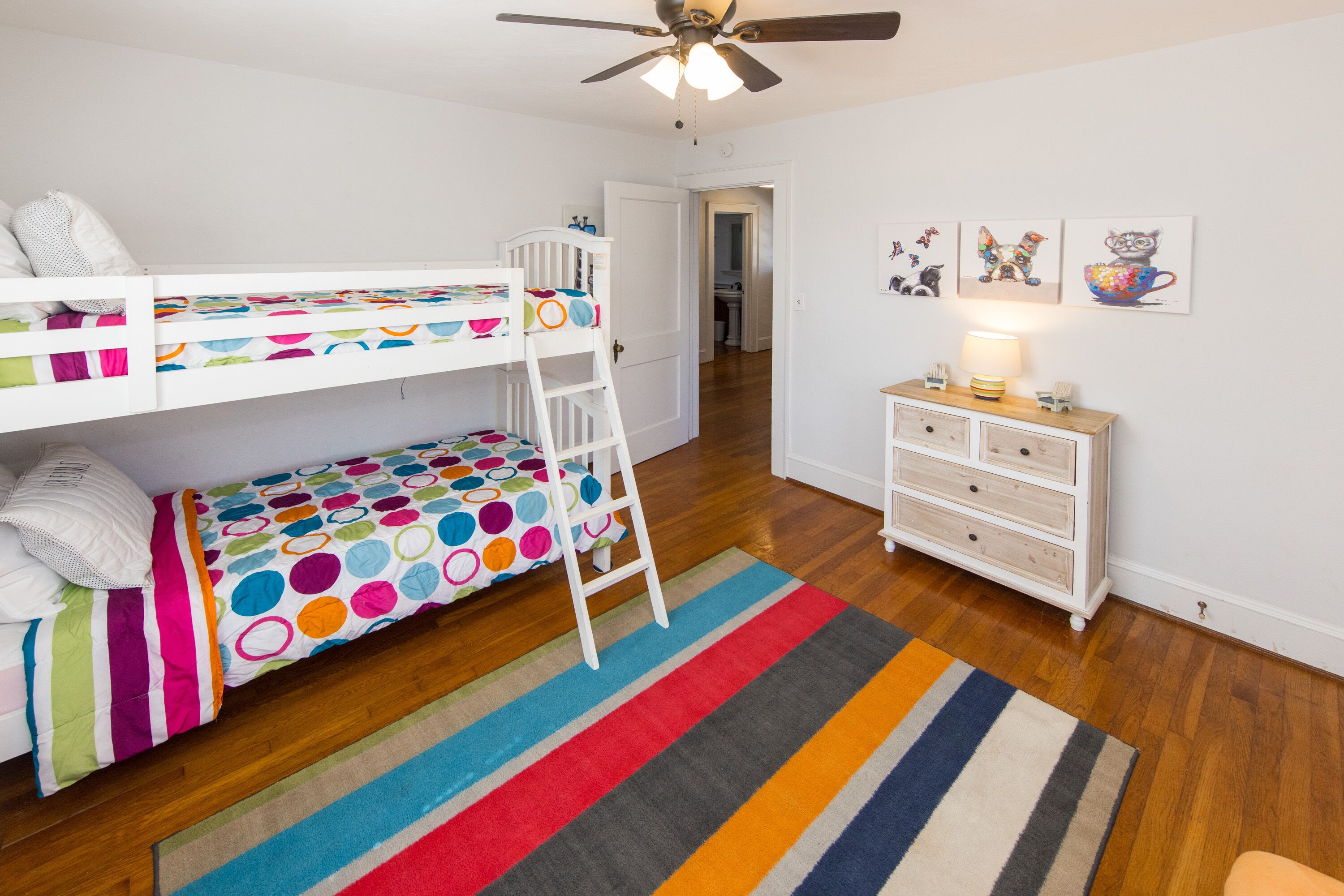 Een kinderkamer met stapelbedden, een trapje, een dressoir en een kleurrijk vloerkleed.