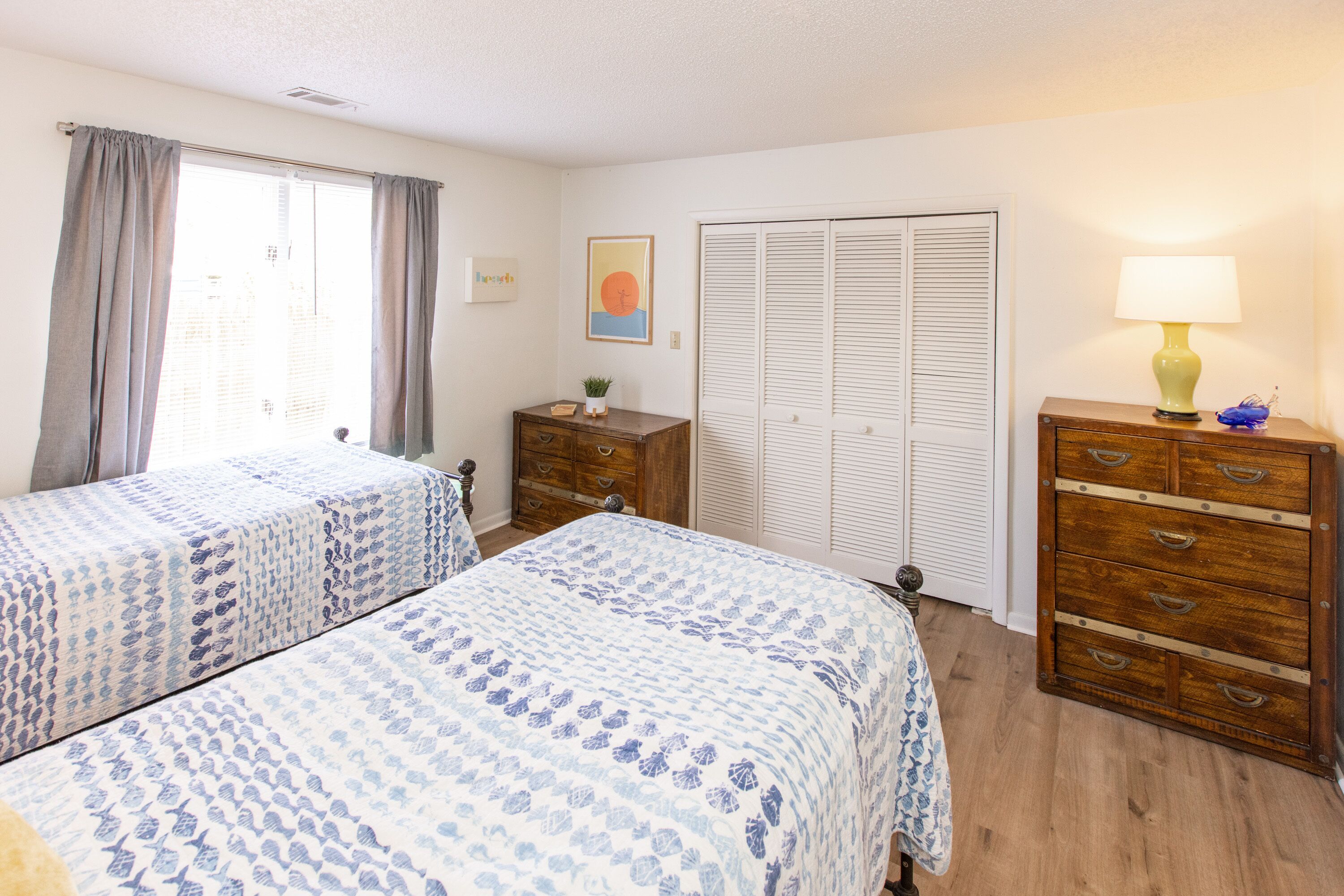 Een slaapkamer met twee bedden, een kaptafel, een lamp, een kast en een raam met gordijnen.
