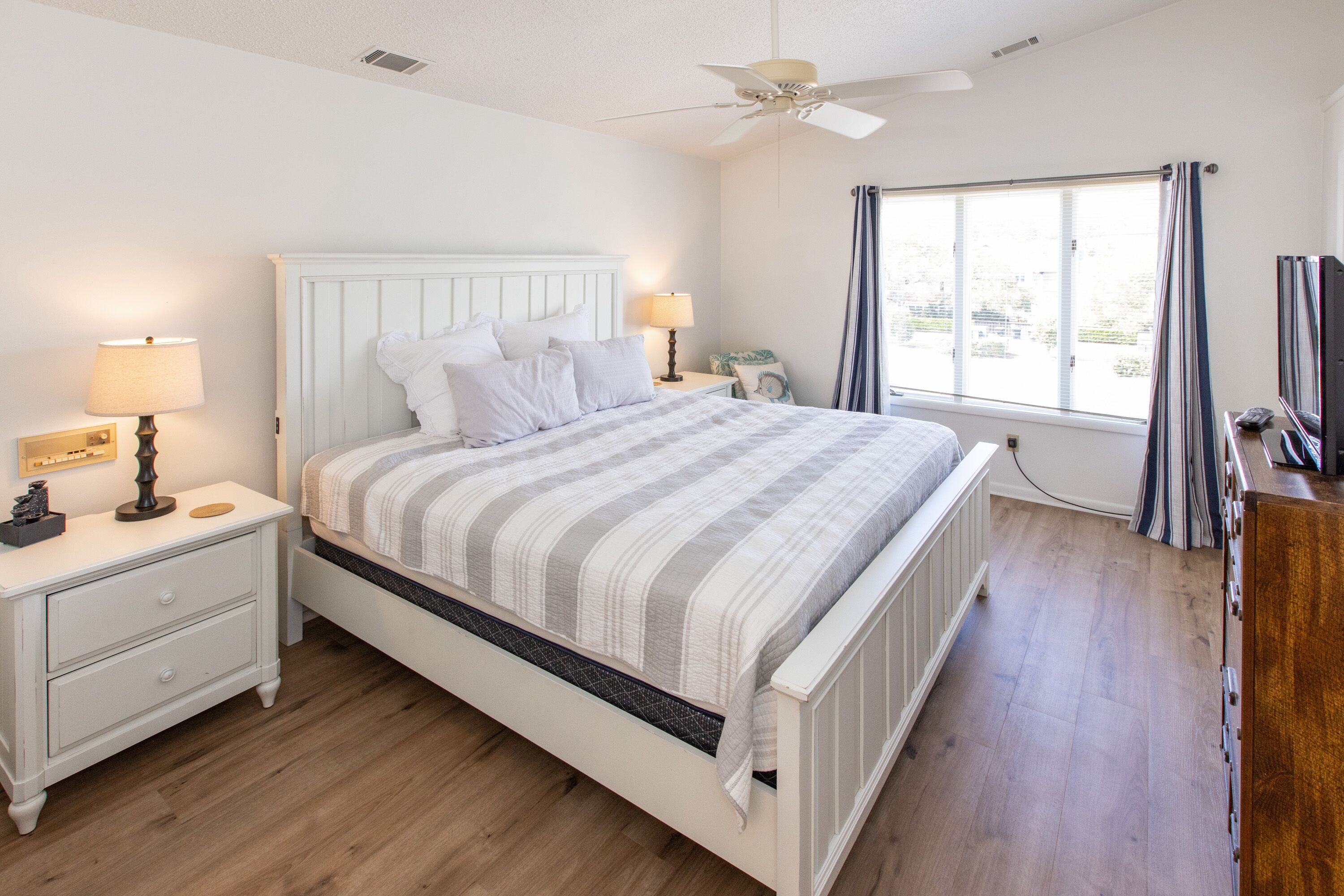 A bedroom with a bed, nightstands, a ceiling fan, and a window with curtains.