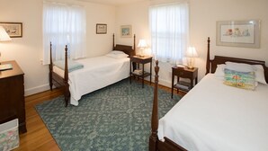 Ett hotellrum med två separata sängar, en byrå i trä, ett nattduksbord med en lampa och en blå, mönstrad matta.