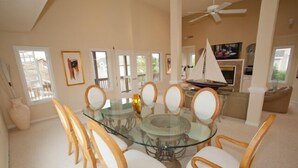 A dining area with a glass table surrounded by wicker chairs, a ceiling fan, and a sailboat model on the table. - A Wave From It All - Croatan VB (Virginia Beach)