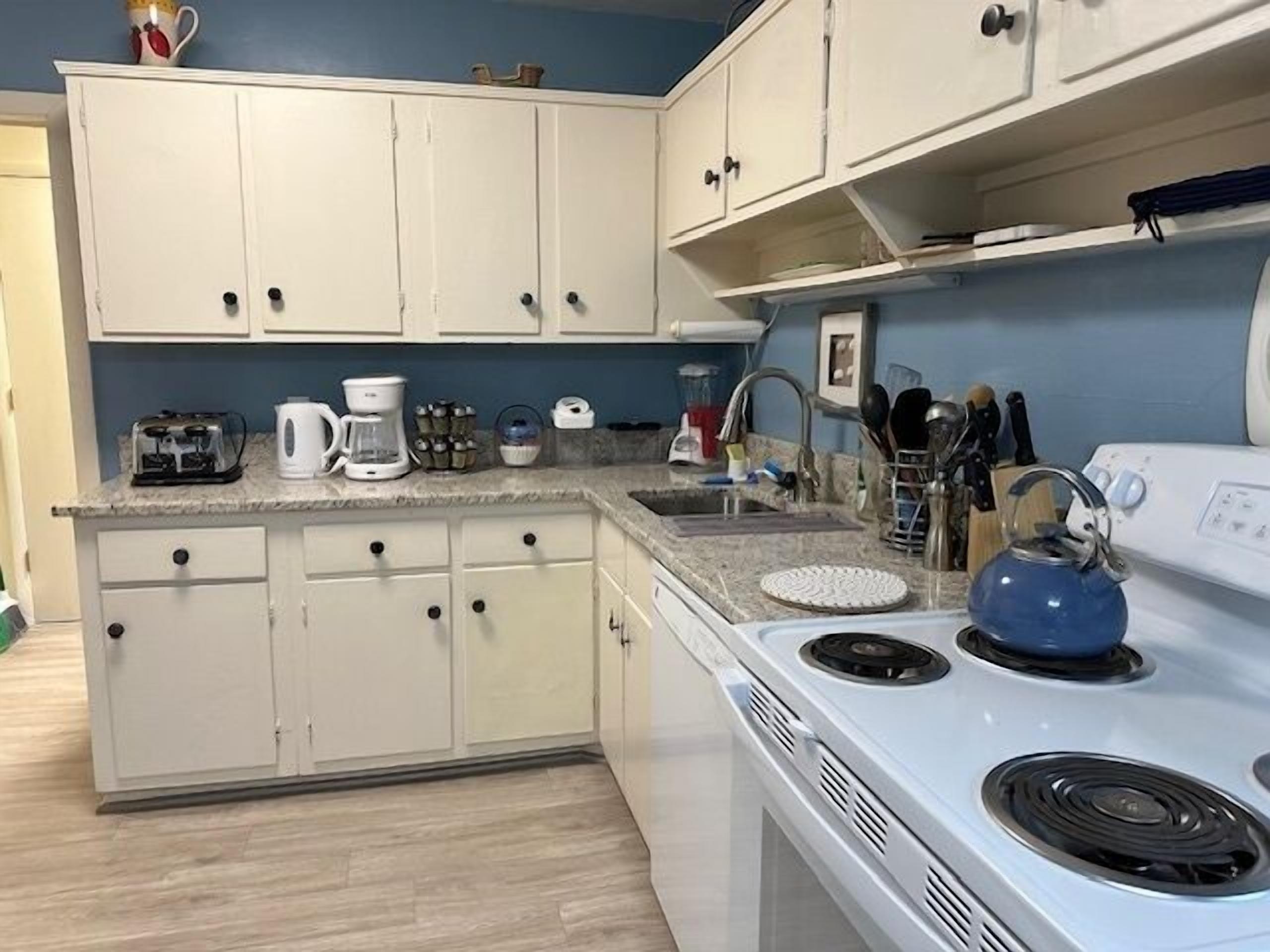 Una cocina con armarios blancos, una estufa blanca y varios electrodomésticos, como una cafetera y un tostador.