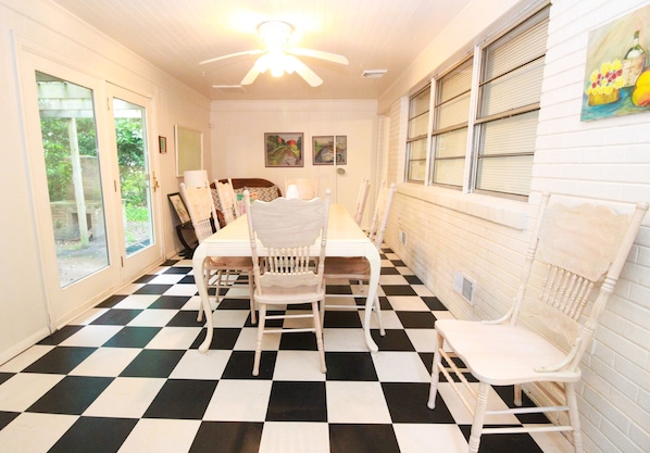 A dining area with a checkered floor, white chairs, a table, and a ceiling fan.
