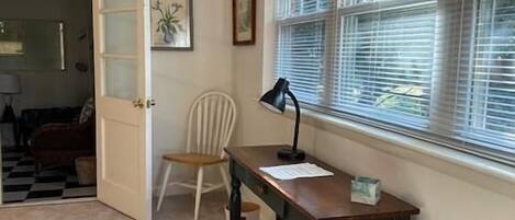 A room with a desk, chair, window with blinds, and a door leading to another room.