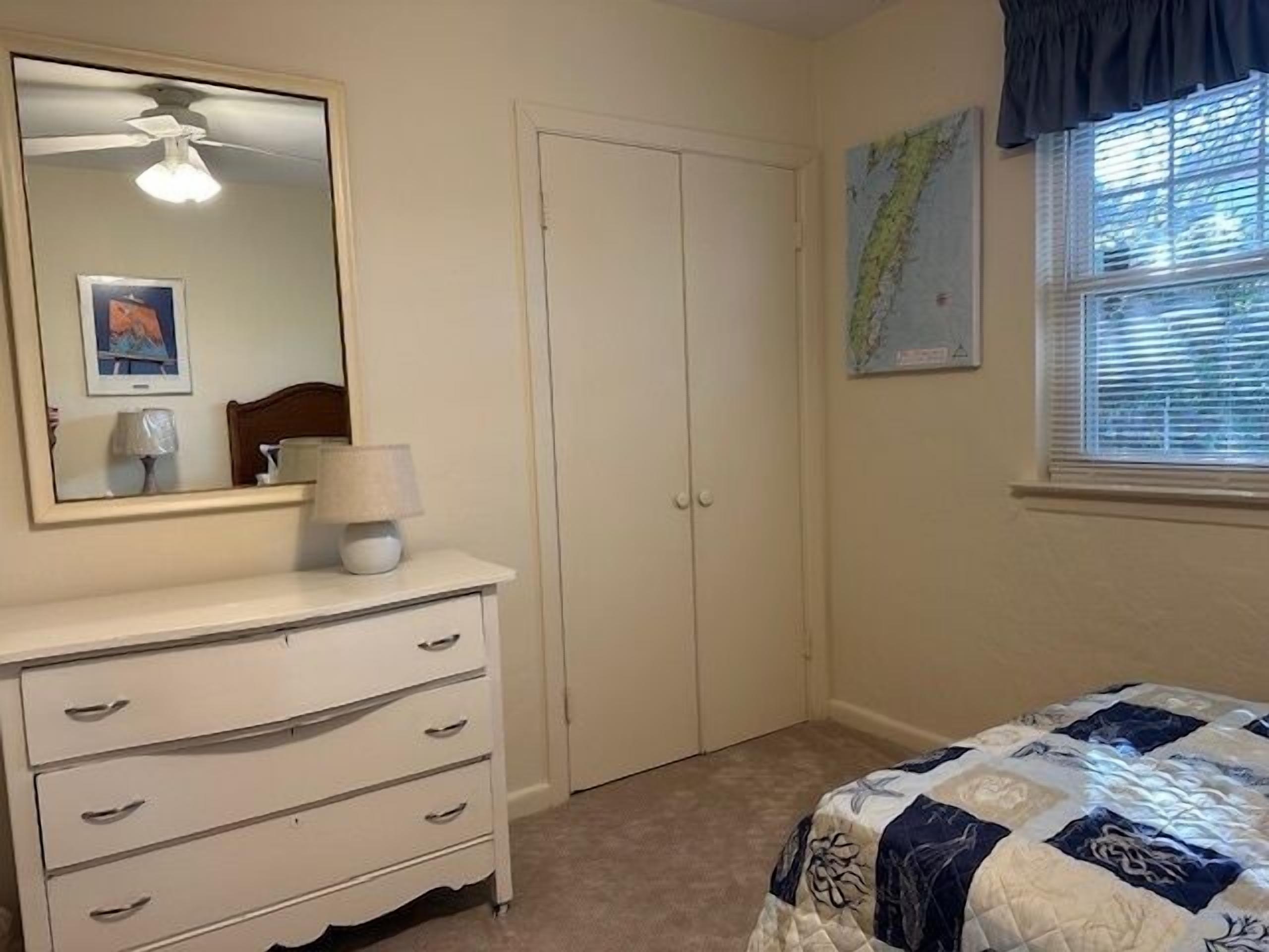 A bedroom with a bed, a dresser, a mirror, a ceiling fan, and a window with blinds.