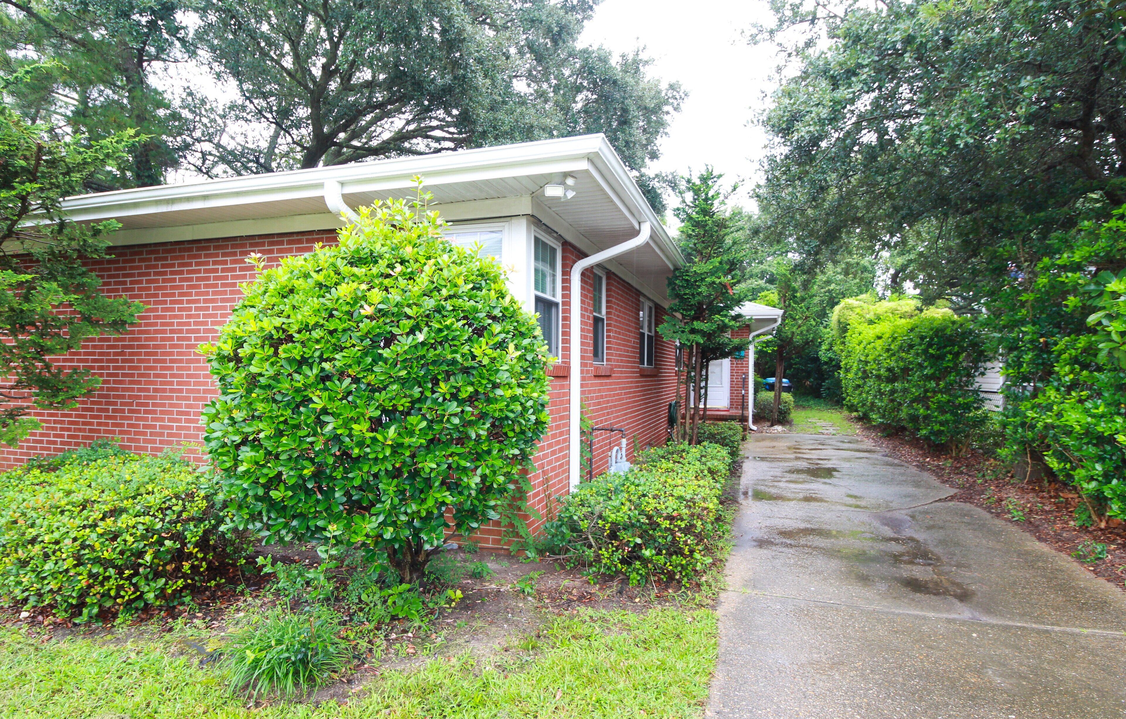 A red brick house with a white front door, surrounded by lush green bushes and trees.