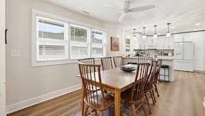 Un coin repas avec une table et des chaises en bois, un ventilateur de plafond, et une cuisine dotée de meubles blancs et d’un four à micro-ondes.