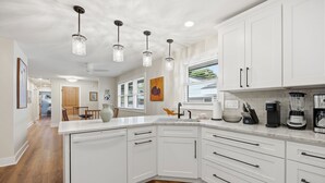 Une cuisine moderne avec des meubles blancs, un lave-vaisselle, un évier et un plan de travail sur lequel se trouvent une machine à café et un mixeur.