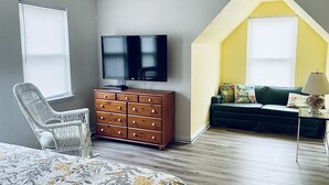 Une chambre à coucher comprenant un lit, une commode, un téléviseur et un petit coin salon avec un canapé et une lampe.