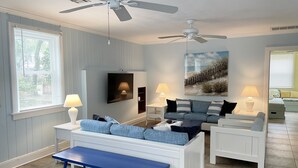 Un salon avec un canapé blanc, un banc bleu et un ventilateur de plafond.