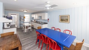 A compact kitchen with white cabinets, a blue dining table, and red chairs. - Sea Home - North End VB (Virginia Beach)