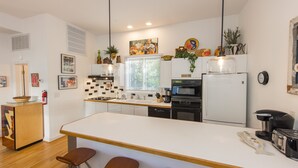 A modern kitchen with a central island, bar stools, a refrigerator, oven, and a coffee machine. - Fairbanks House with beach access just steps from your front door (Virginia Beach)