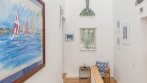 A staircase with wooden steps and a handrail, leading to a landing with a framed painting, a decorative fish sculpture, and a small table with a chair. - Fairbanks House with beach access just steps from your front door (Virginia Beach)