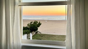 Uitzicht vanuit een raam op een strand bij zonsondergang.