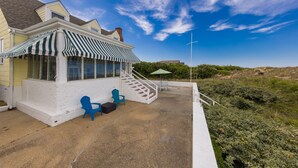 A white building with a striped awning, outdoor seating, and a staircase leading to a covered area. - Harshaw Beach House - North End Oceanfront (Virginia Beach)