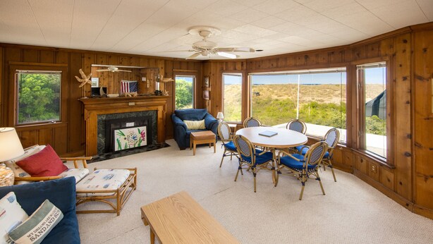 A cozy room with a fireplace, a blue sofa, a wooden bench, and a dining table with chairs. - Harshaw Beach House - North End Oceanfront (Virginia Beach)