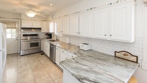 A kitchen with white cabinets, a stainless steel oven, a marble countertop, and a wooden stool. - Harshaw Beach House - North End Oceanfront (Virginia Beach)