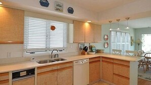 A kitchen with wooden cabinets, a dishwasher, a sink, and a window with blinds. - Dolphin's Den - Oceanfront - North End VB (Virginia Beach)