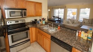 Una cocina moderna con encimeras de granito, electrodomésticos de acero inoxidable, armarios de madera y una zona de comedor con sofá y mesa.