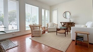 A spacious living room with large windows, a white sofa, a wooden coffee table, and a woven rug. - Turtle Cove - North End VB (Virginia Beach)