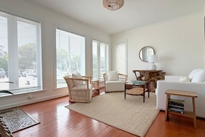 A spacious living room with large windows, a white sofa, a wooden coffee table, and a woven rug. - Turtle Cove - North End VB (Virginia Beach)