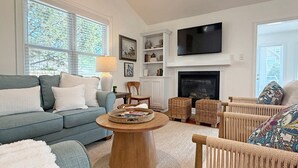 A living room with a sofa, a coffee table, wicker chairs, a fireplace, and a television. - Turtle Cove - North End VB (Virginia Beach)