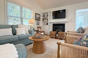 A living room with a sofa, a coffee table, wicker chairs, a fireplace, and a television. - Turtle Cove - North End VB (Virginia Beach)