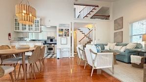 A spacious living area with a dining table, chairs, a sofa, and a staircase leading to an upper level. - Turtle Cove - North End VB (Virginia Beach)