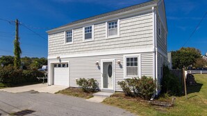 A two-story house with a garage, a front door, and a small front yard with bushes. - Conch Shell Cottage - North End VB (Virginia Beach)