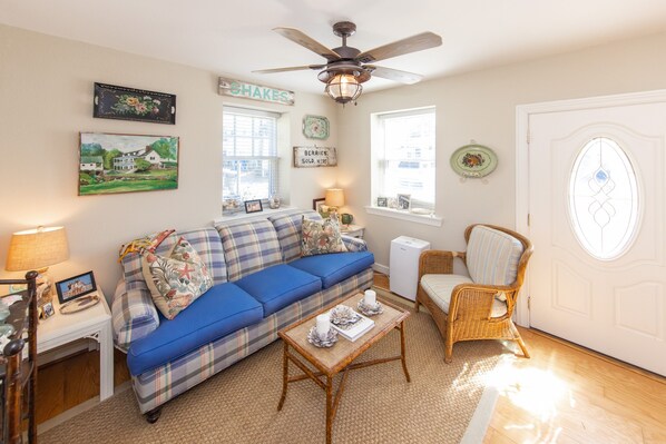 A cozy living room with a blue sofa, a wicker chair, a coffee table, and a ceiling fan.