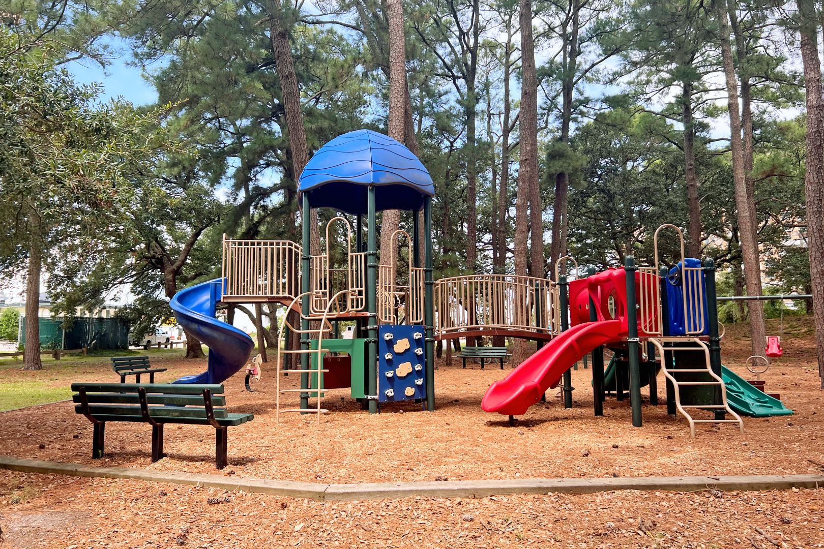 A playground with a blue slide, red slide, and climbing structures surrounded by trees.