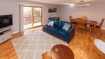 A living room with a blue sofa, a wooden dining table, and a TV.