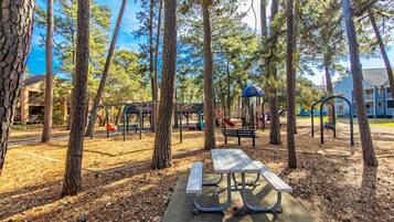 A park with playground equipment, a picnic table, and trees.
