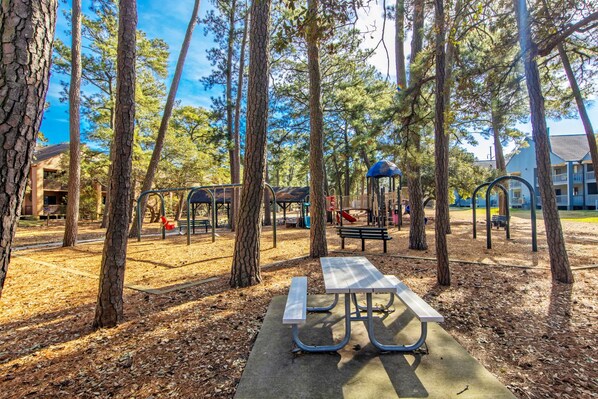 A park with playground equipment, a picnic table, and trees.