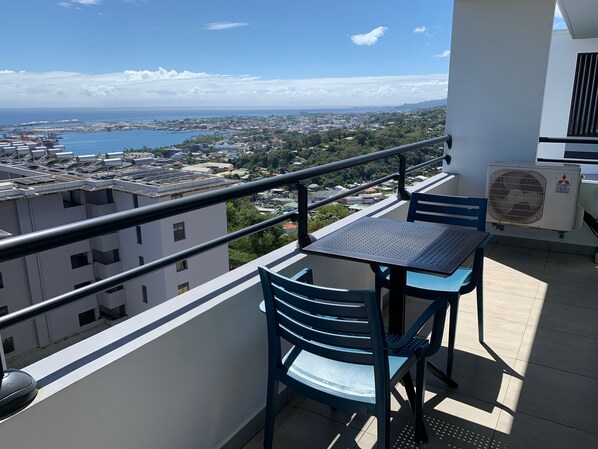 Un balcón con mesa y sillas, con vistas a un paisaje urbano con edificios y una masa de agua.