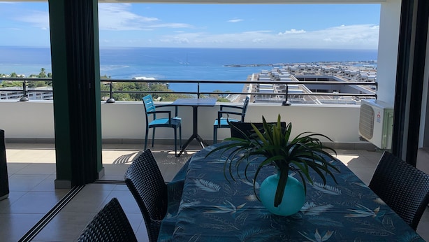 A balcony with a table and chairs, overlooking a cityscape and the sea.