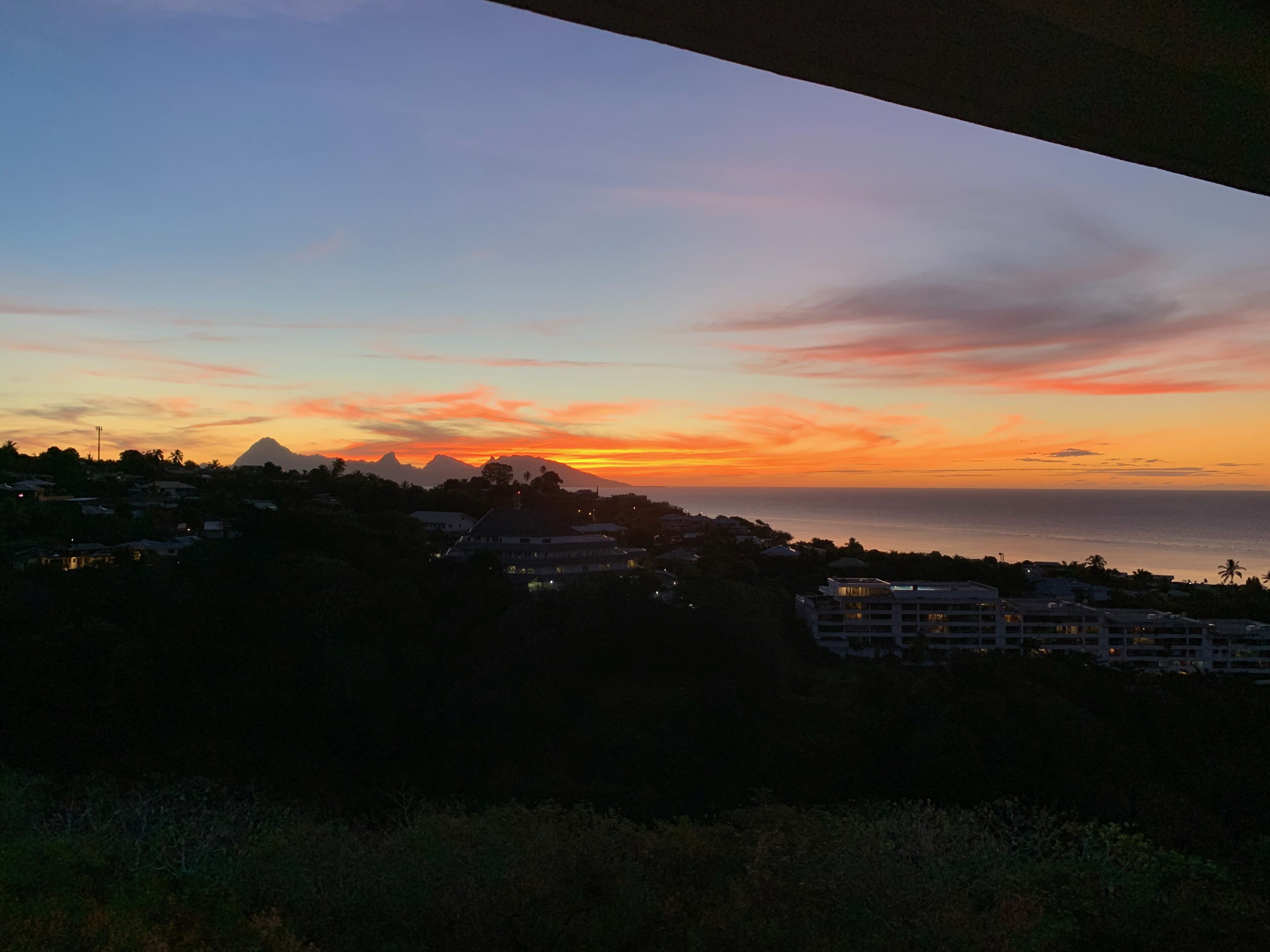 A coastal landscape at sunset with a mountain in the background and buildings along the shore.