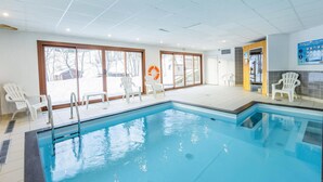 An indoor swimming pool with clear glass walls, white chairs, and a lifebuoy. - Nice apartment in Saint-Pancrace with sauna (Saint-Pancrace)