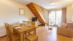 A dining area with a wooden table and chairs, a TV on a small table, and a staircase leading to a balcony. - Nice apartment in Saint-Pancrace with sauna (Saint-Pancrace)