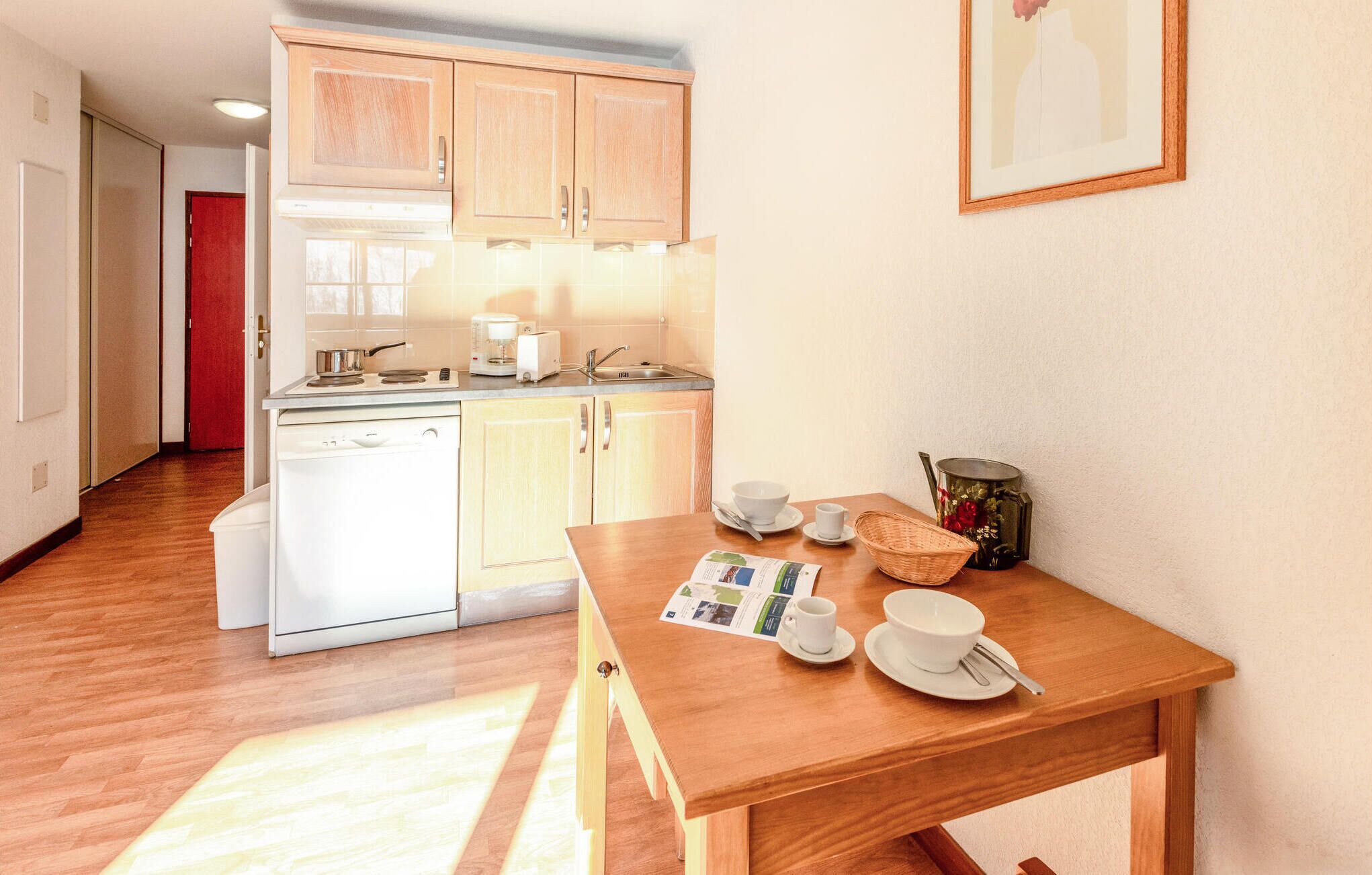 Cocina compacta con armarios de madera, lavavajillas integrado y zona de comedor con mesa de madera para dos personas.