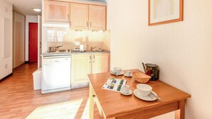 A compact kitchen with wooden cabinets, a built-in dishwasher, and a dining area with a wooden table set for two. - Nice apartment in Saint-Pancrace with sauna (Saint-Pancrace)