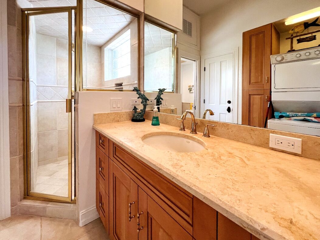 A bathroom with a large sink, wooden cabinets, a glass shower enclosure, and a mirror.