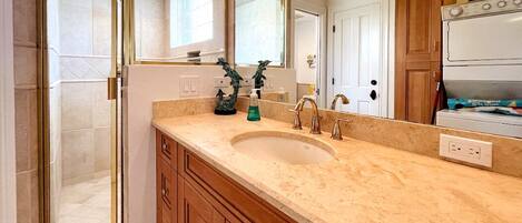 A bathroom with a large sink, wooden cabinets, a glass shower enclosure, and a mirror.