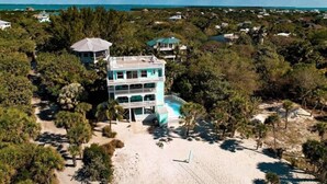 A multi-story building with a pool, surrounded by dense vegetation and a beach.