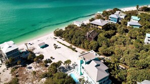 An aerial view of a coastal property with a beach, multiple buildings, and a swimming pool.